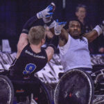 this picture shows two rugby wheelchair athletes reaching for the ball