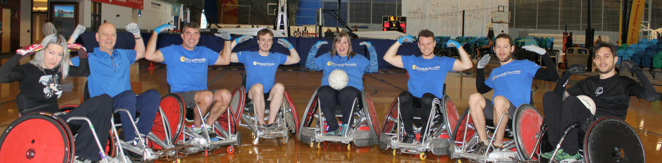this picture shows Pinnacle Pursuits Team lined up sittting on Rugby Wheelchairs flanked by tow Rugby Wheelchair pros Terri and Trevor while flexing their arms