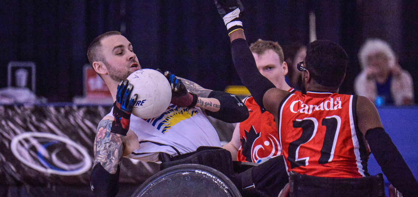 BC Wheelchair Rugby athlete leaning back to fend off two opponents
